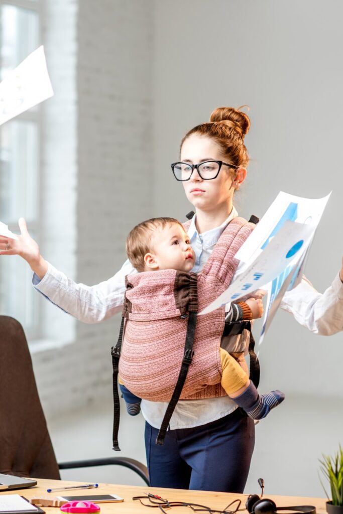 Signs you’re doing to much as a mum, overwhelmed mum throwing paper with baby on her front